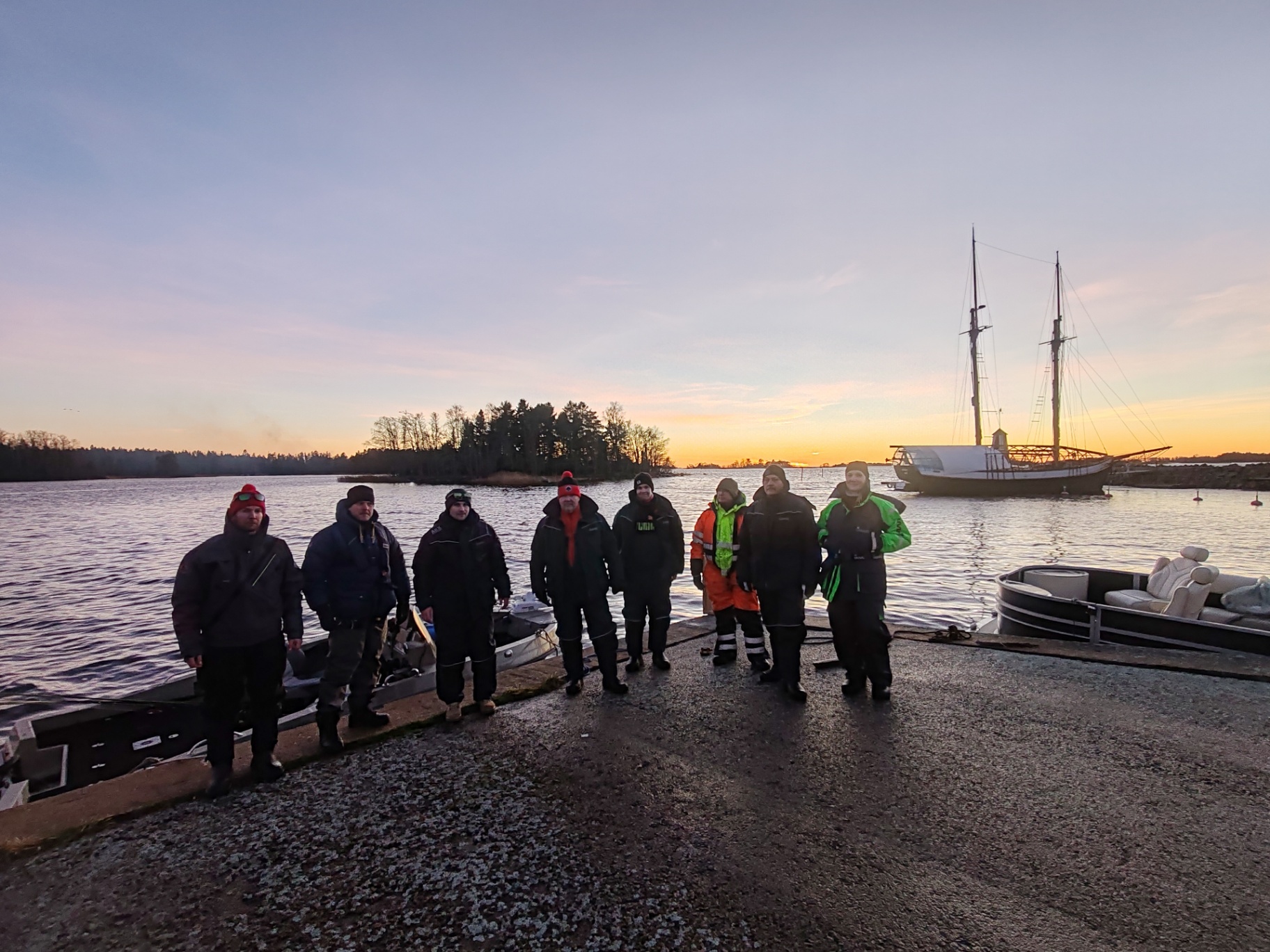 Ryhmä rannassa auringonlaskussa purjealuksen kanssa